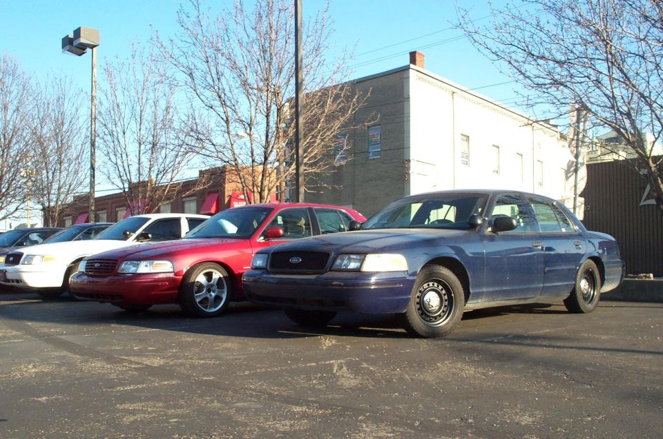 Several Ford Crown Victoria police cars parked in a lot. One is dark blue, others are red and white