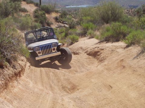 1993 Ford Bronco - A Jeep Wrangler TJ navigates a steep, sandy off-road trail with a dry, hilly landscape in the background.