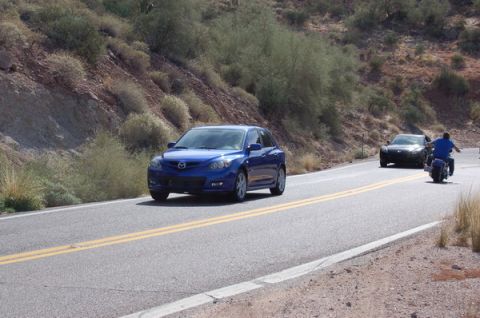 2006 Mazda RX-8 - A blue Mazda 3 hatchback is seen on a desert highway, followed by another car and a motorcycle.