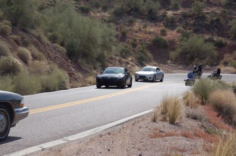 2006 Mazda RX-8 - A convoy of vehicles, including a black Mazda RX-8 and a silver sports car, travels along a winding road.