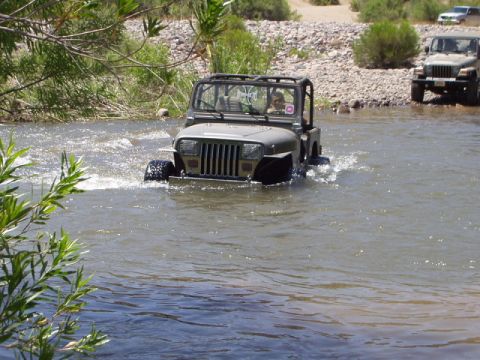 1993 Ford Bronco - A gray Jeep Wrangler navigates a shallow river, with another Jeep visible further upstream.