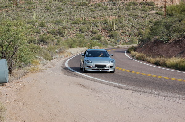 Silver Mazda RX-8 driving on a curving desert highway lined with saguaro cactus