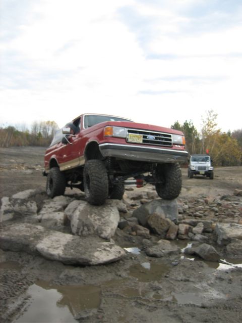 2002 Jeep Wrangler - A red Ford Bronco tackles a rocky obstacle course, while another Jeep observes from the background.
