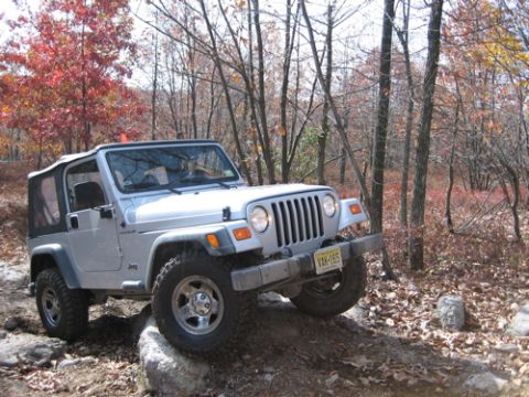 2002 Jeep Wrangler - 2002 Jeep Wrangler navigating a rocky path in a forest during autumn.