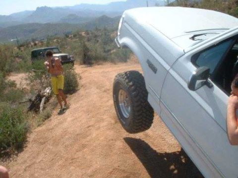 1993 Ford Bronco - A white 1993 Ford Bronco navigates a dusty off-road trail with a person standing nearby.