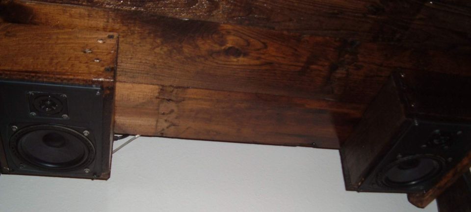 Two black speakers are mounted beneath a dark wooden beam