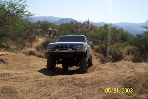1993 Ford Bronco - A modified Ford Bronco navigates a sandy trail with mountains in the background.