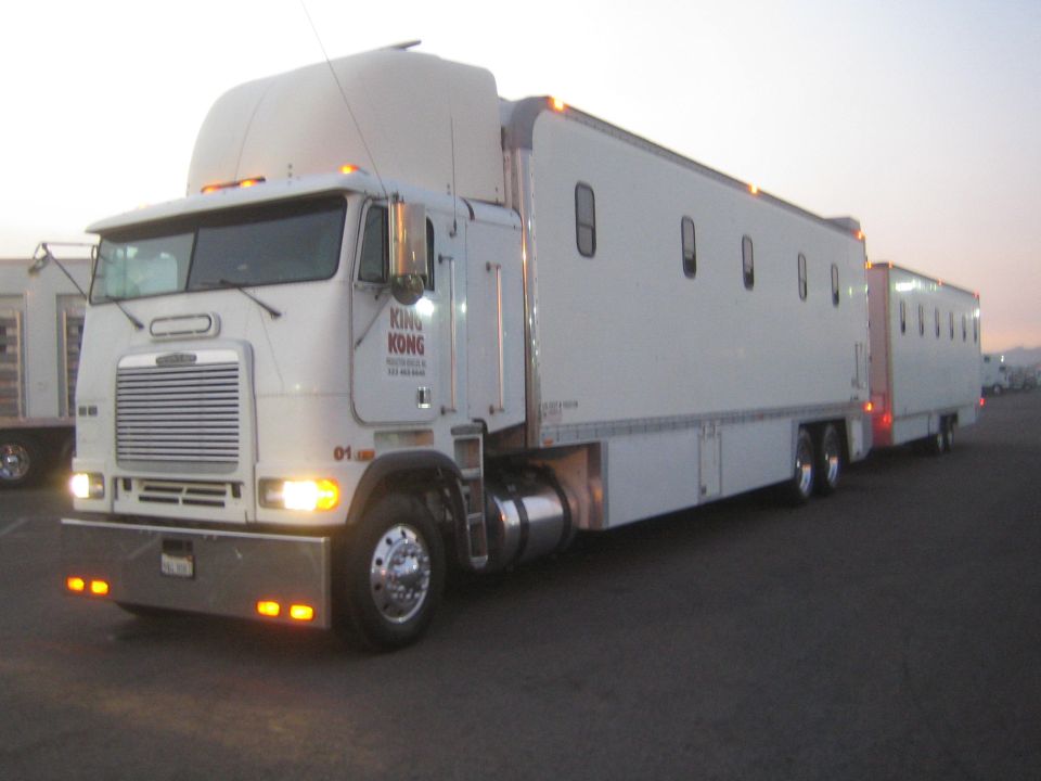 White cabover Freightliner semi truck with chrome grille and trailers parked at dawn