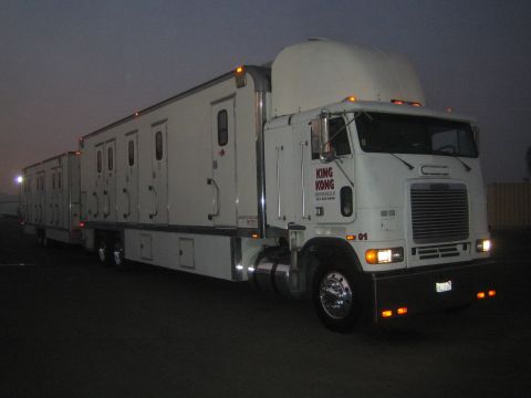 1990 Ford Bronco - Side view of a white cabover semi truck and its long sleeper trailer rig parked in a lot at dusk with marker lights lit.