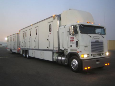 1990 Ford Bronco - Angled view of a white cabover semi pulling sleeper trailers in an open lot, headlights and marker lights illuminated at dawn.