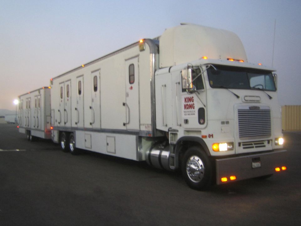 White cabover semi truck pulling sleeper trailers, angled side view at dawn in an open lot