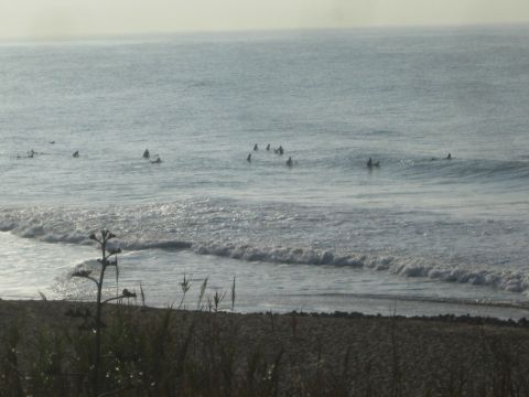 1990 Ford Bronco - group of surfers waits in the lineup beyond a breaking wave, viewed from a grassy coastal bluff.