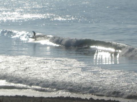 1990 Ford Bronco - lone surfer rides the face of a sunlit, glistening wave as whitewater breaks toward the beach.