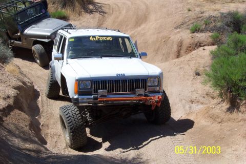 1993 Ford Bronco - Two Jeeps navigate a steep, sandy off-road trail with sparse vegetation.