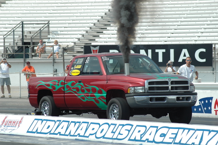 Red Dodge Ram diesel drag truck with green flames belching black smoke at Indianapolis Raceway starting line