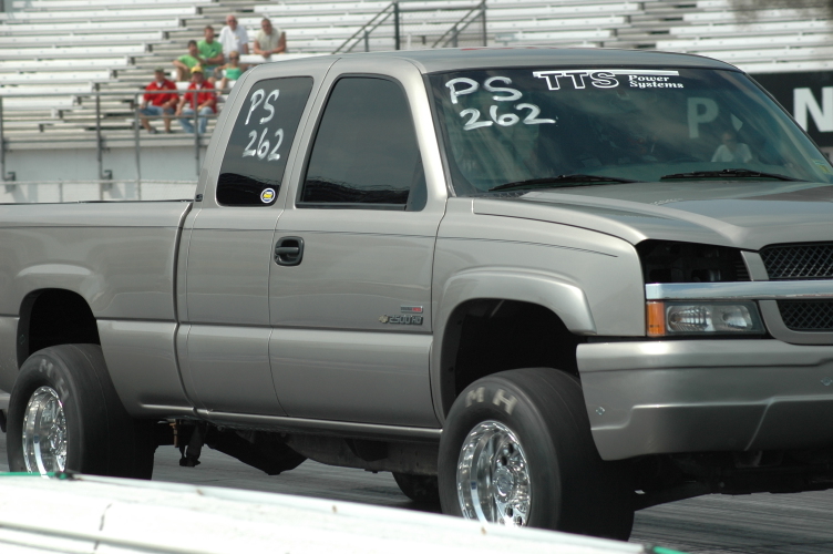 Silver extended-cab pickup with PS 262 windshield markings and M/H drag tires at a drag strip