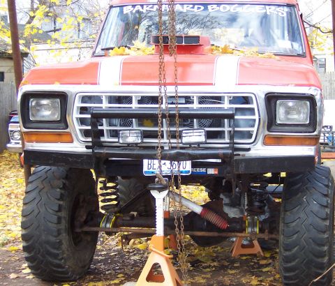 1978 Ford Bronco - Modified 1978 Ford Bronco front end, lifted and supported by jack stands, with 'BARNHARD BOGGERS' text on windshield.