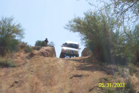 1993 Ford Bronco - A white SUV navigates a challenging off-road trail on a sunny day.