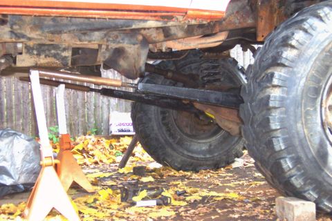 1978 Ford Bronco - The underside of a vehicle is shown, with large tires and suspension parts visible, resting on jack stands.