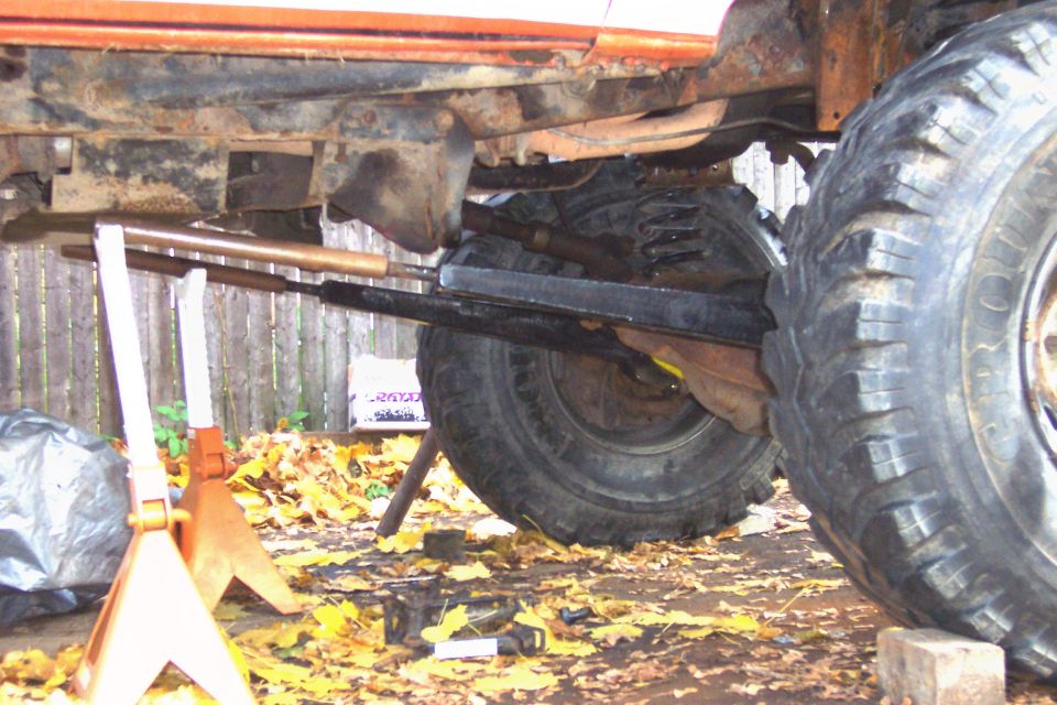 Undercarriage of a vehicle with large tires, jack stands, and suspension components visible