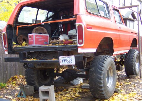 1978 Ford Bronco - Orange 1978 Ford Bronco lifted with large tires, parts visible in the open tailgate.