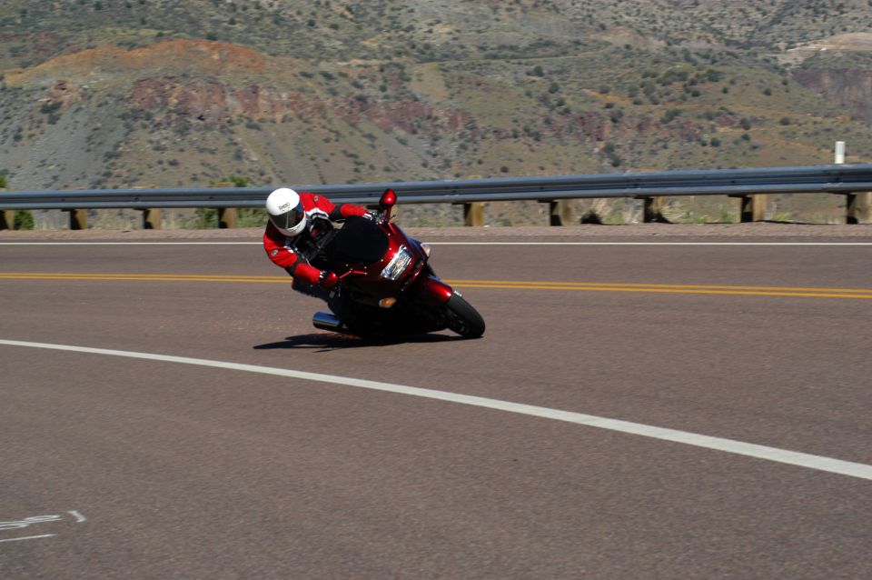 Rider in red leathers leaning a dark red sportbike hard through a corner on a mountain highway