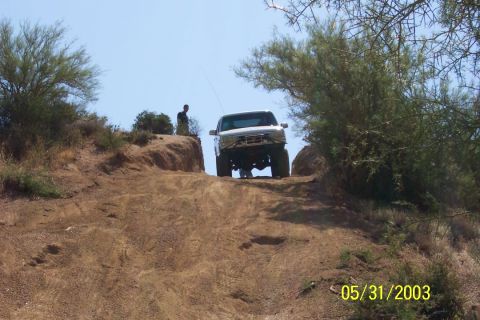 1993 Ford Bronco - A white 1993 Ford Bronco navigates an off-road dirt incline under a clear blue sky.