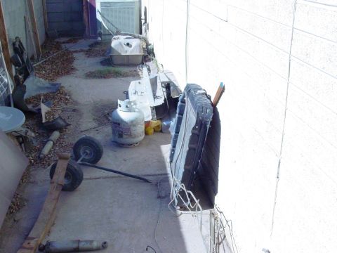1979 Ford Bronco - A collection of automotive parts and a propane tank are stored outdoors next to a building.