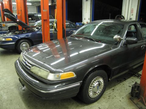 1991 Ford LTD Crown Victoria - Two Ford Crown Victorias are parked inside a garage, one dark gray and one blue.