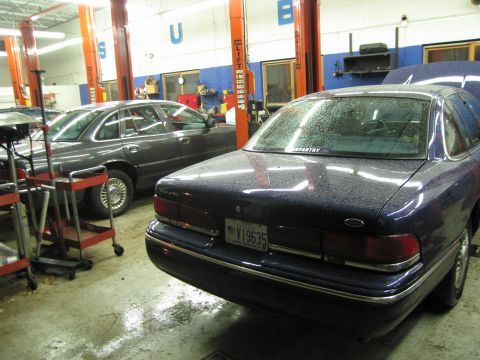 1991 Ford LTD Crown Victoria - Two Ford Crown Victorias are parked in a service bay, one dark blue and the other grey.