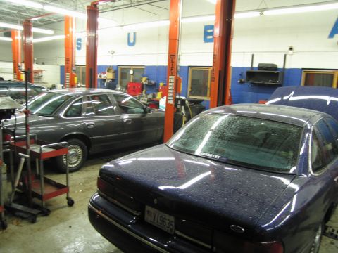 1991 Ford LTD Crown Victoria - Two sedans are parked in a garage with car lifts visible in the background.