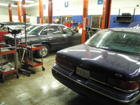 1991 Ford LTD Crown Victoria - Two sedans are parked in a repair shop, one in the foreground and another to the left.