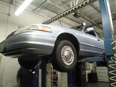 1991 Ford LTD Crown Victoria - A light blue sedan is raised on a car lift inside a service bay.