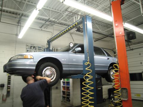 1991 Ford LTD Crown Victoria - Mechanic works on a 1991 Ford Crown Victoria LTD being serviced on a car lift in a garage.