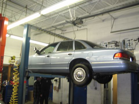 1991 Ford LTD Crown Victoria - A light blue sedan is elevated on a car lift inside a garage, revealing its underside.