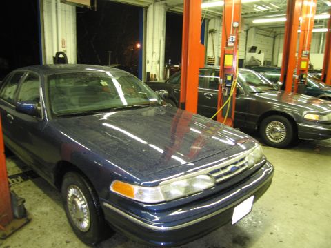 1991 Ford LTD Crown Victoria - Two Ford Crown Victorias are parked in a service bay, one in the foreground.