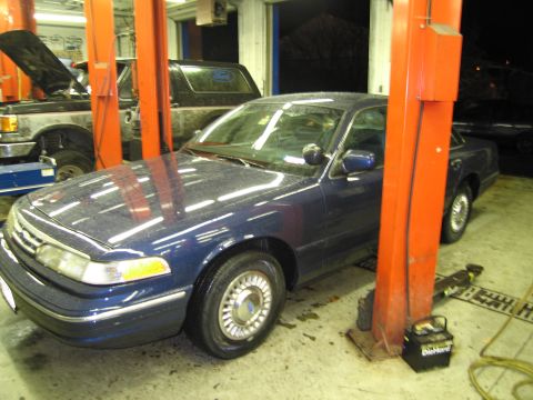1991 Ford LTD Crown Victoria - A blue 1991 Ford Crown Victoria is on a lift in a garage, with another vehicle visible behind it.