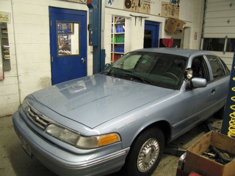 1991 Ford LTD Crown Victoria - A light blue sedan is parked in a garage, possibly for service.