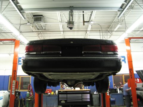 1991 Ford LTD Crown Victoria - A black sedan is raised on a lift in a service bay, showing its undercarriage and rear end.