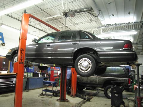 1991 Ford LTD Crown Victoria - A dark gray sedan is elevated on a car lift in a service bay, with another vehicle positioned underneath.