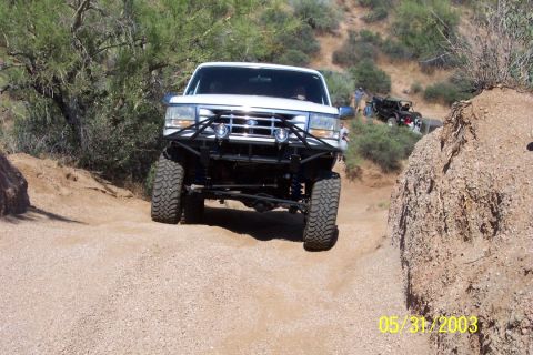1993 Ford Bronco - A white Ford Bronco navigates a rocky off-road path with another vehicle visible in the background.