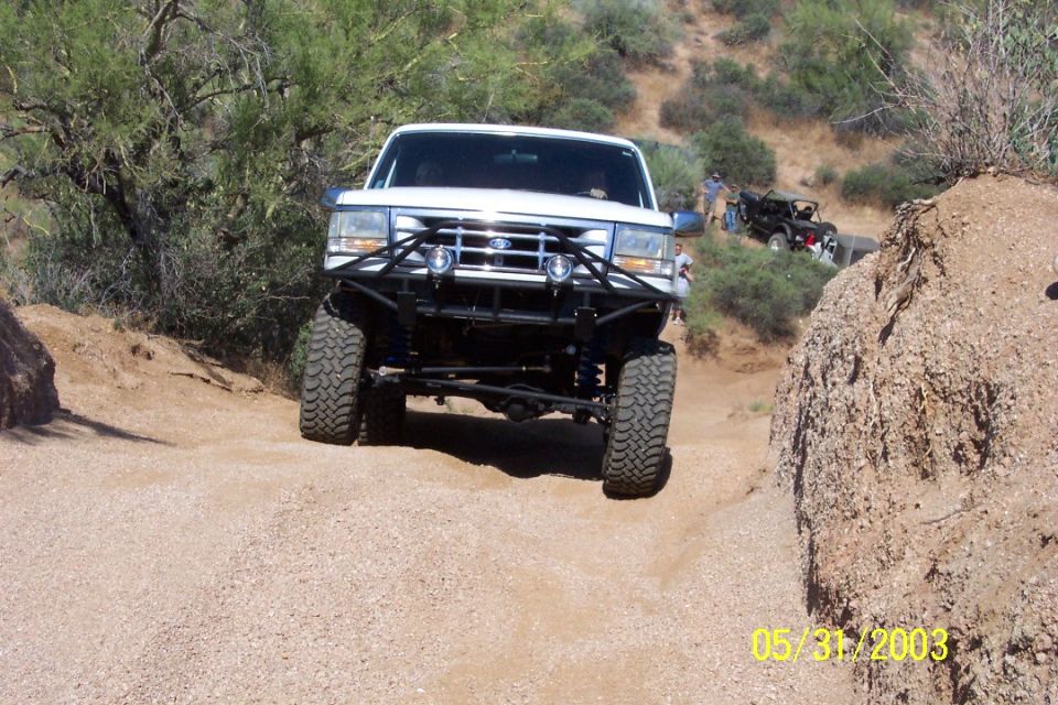 Lifted white Ford Bronco with black tube bumper descending a sandy desert trail