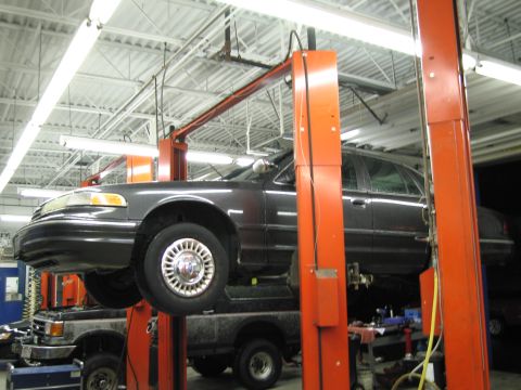 1991 Ford LTD Crown Victoria - A dark sedan is raised on a car lift in a garage, with another vehicle underneath.