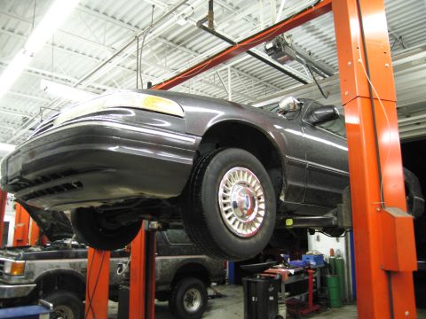 1991 Ford LTD Crown Victoria - A dark sedan is raised on a car lift in a service bay, with another vehicle visible in the background.