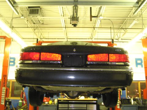 1991 Ford LTD Crown Victoria - The rear of a black 1991 Ford Crown Victoria is shown elevated on a car lift in a service bay.