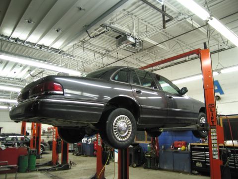 1991 Ford LTD Crown Victoria - Dark colored 1991 Ford Crown Victoria LTD is raised on a hydraulic lift inside a service bay.