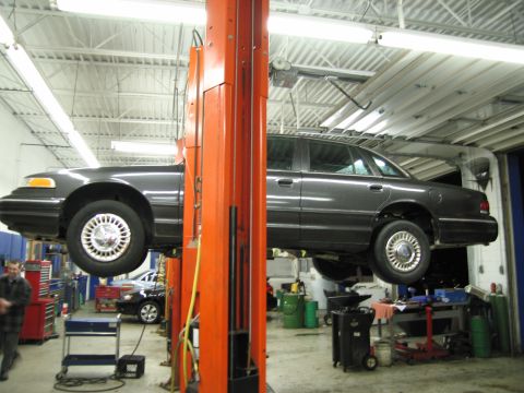 1991 Ford LTD Crown Victoria - A dark sedan is raised on a car lift inside a service bay, with another vehicle in the background.