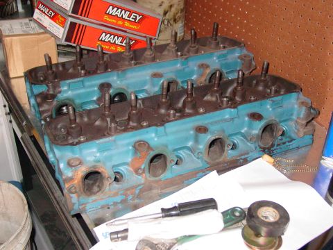 1979 Ford Bronco - Two engine cylinder heads, painted blue, sit on a workbench with tools and boxes of Manley parts.