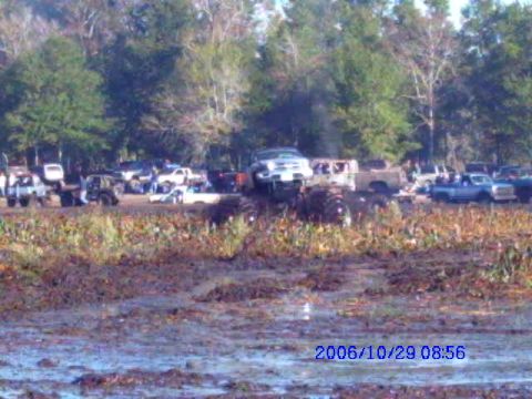 1987 Suzuki Samurai - Several off-road vehicles are seen in a muddy field, with trees in the background.