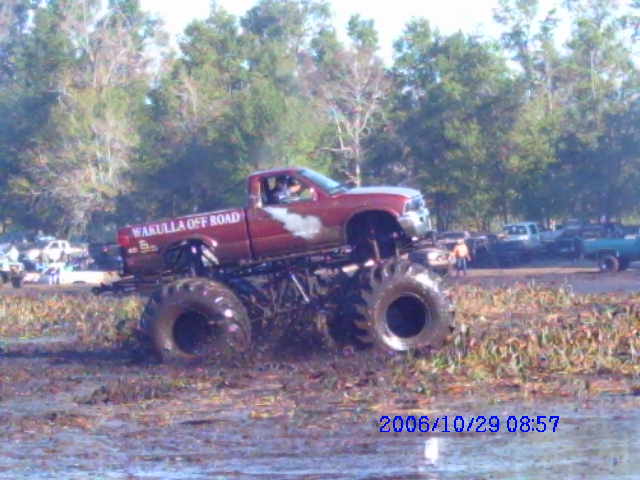 Red monster truck with 'Wakulla Off Road' text on the side, in a muddy field
